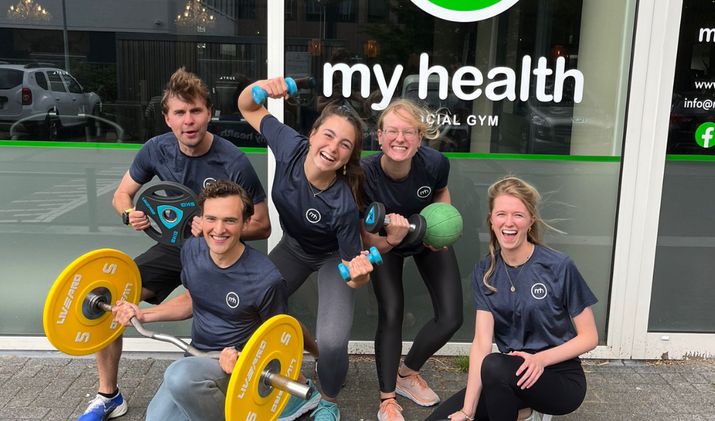 Lachende trainers van MyHealth met gewichten voor de ingang van de sportschool